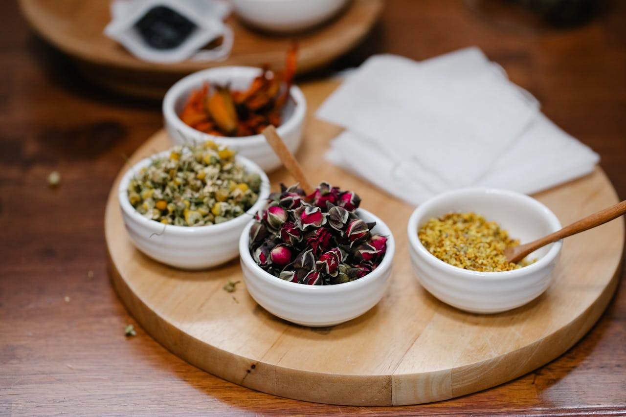 Close-up view of various dried herbs and spices in white bowls on a wooden tray, perfect for culinary arts or natural remedies.